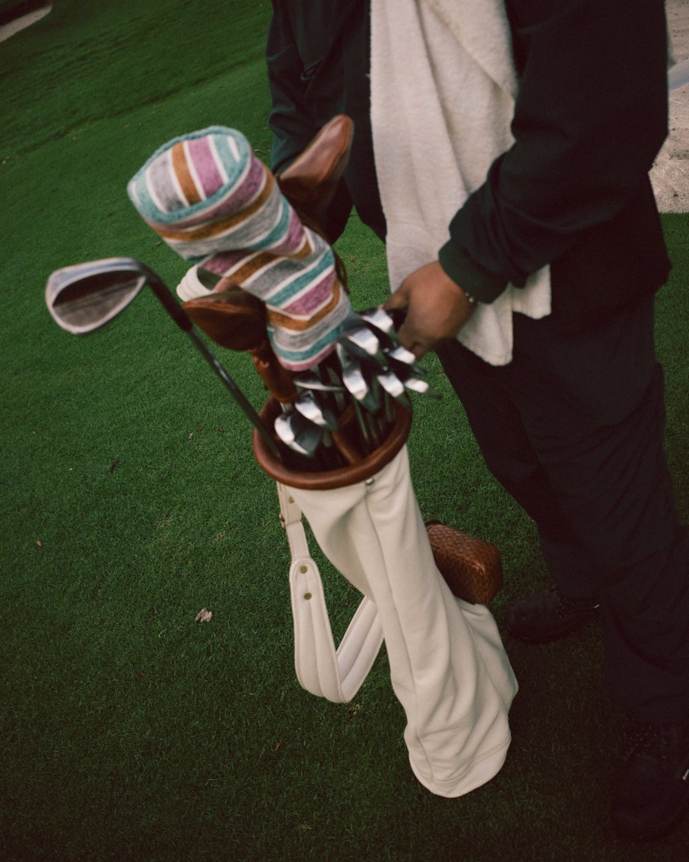 A golfer pulling clubs with striped and leather headcovers from a white bag