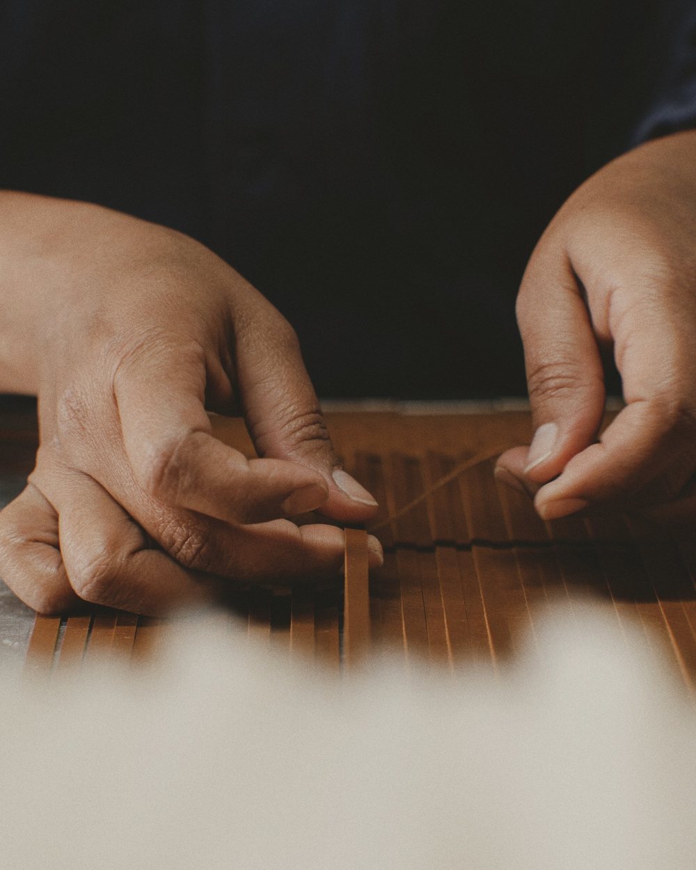Hands working a strip of leather on a workbench