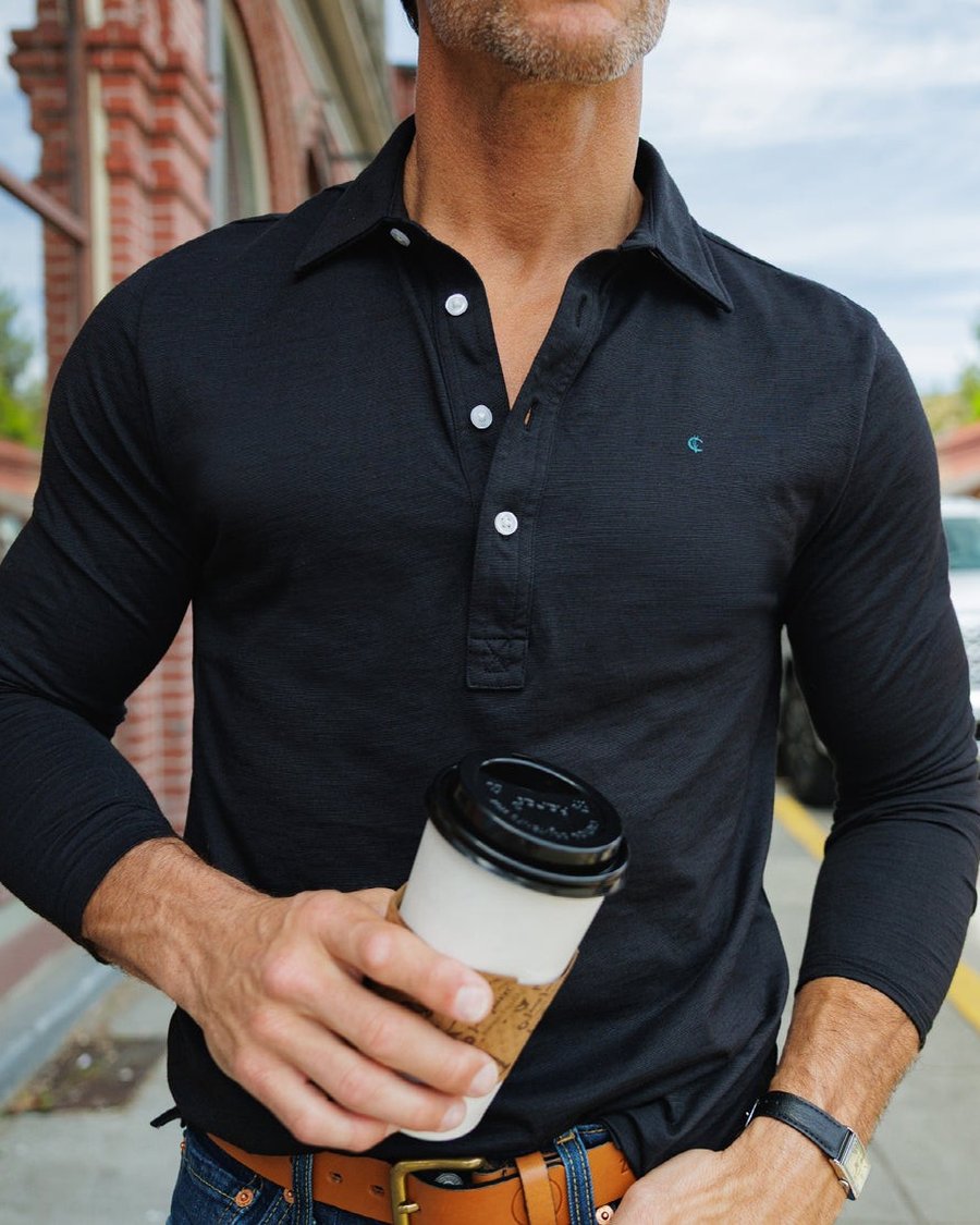 A man in a black Criquet shirt holding a coffee