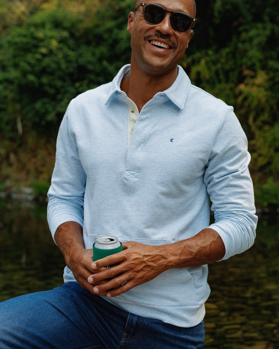 A man in a light blue Criquet shirt holding a drink by the water