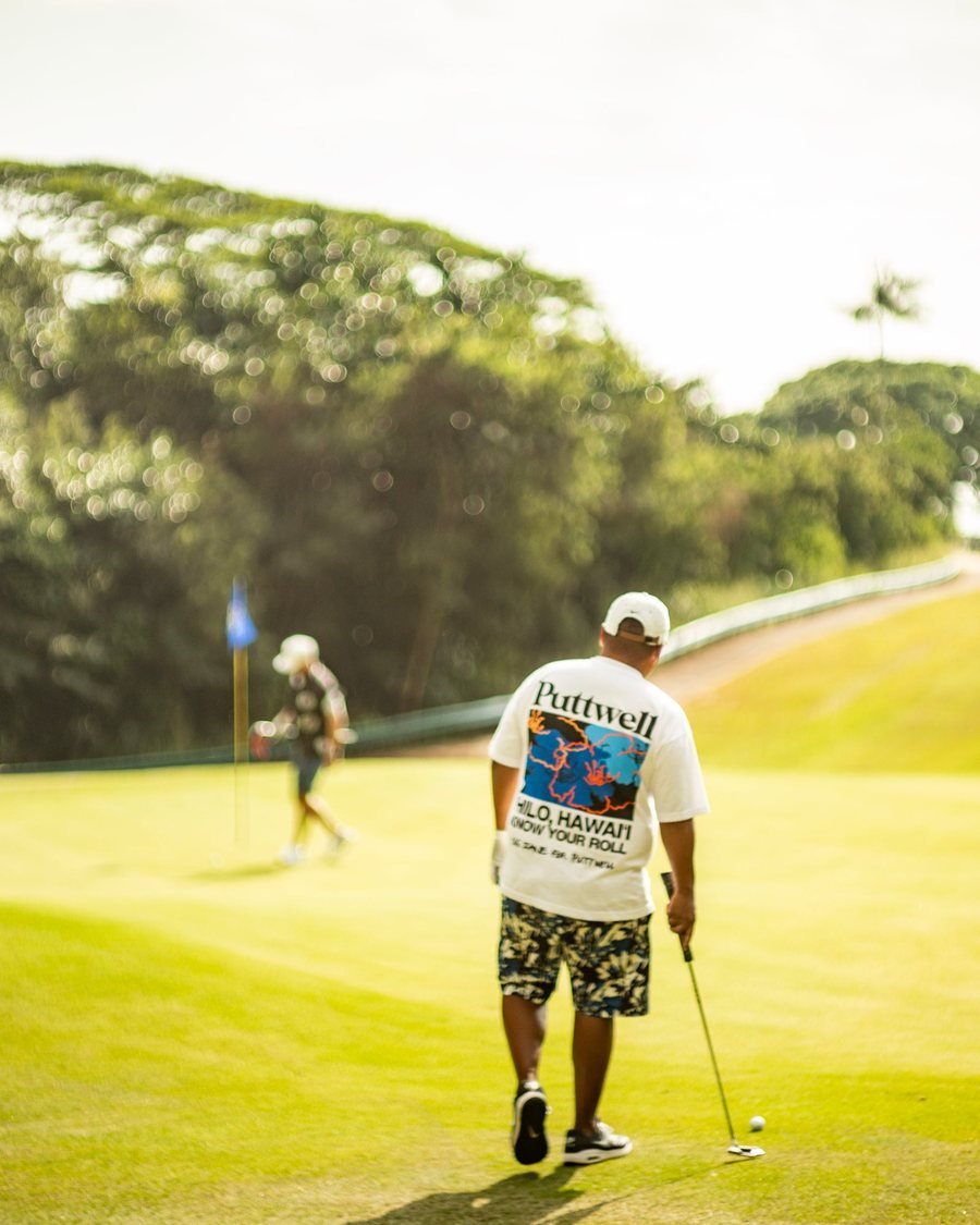 A golfer in a Puttwell tee walking up a green toward the flag
