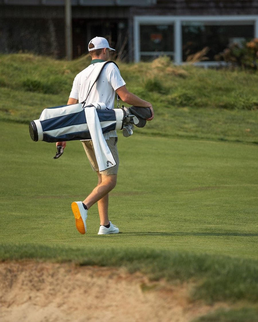 A golfer walking a fairway carrying a navy and white Jones bag