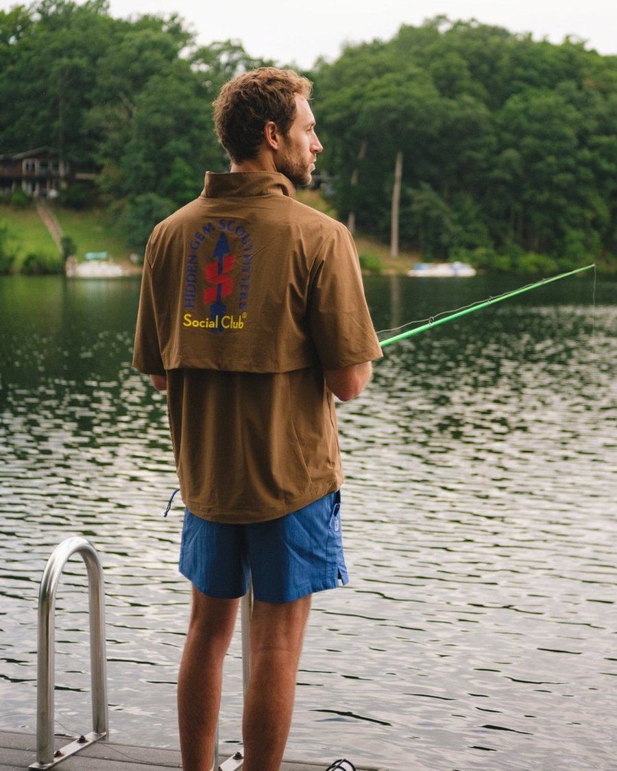 A man in a Sugarloaf Social Club shirt fishing off a dock on a lake