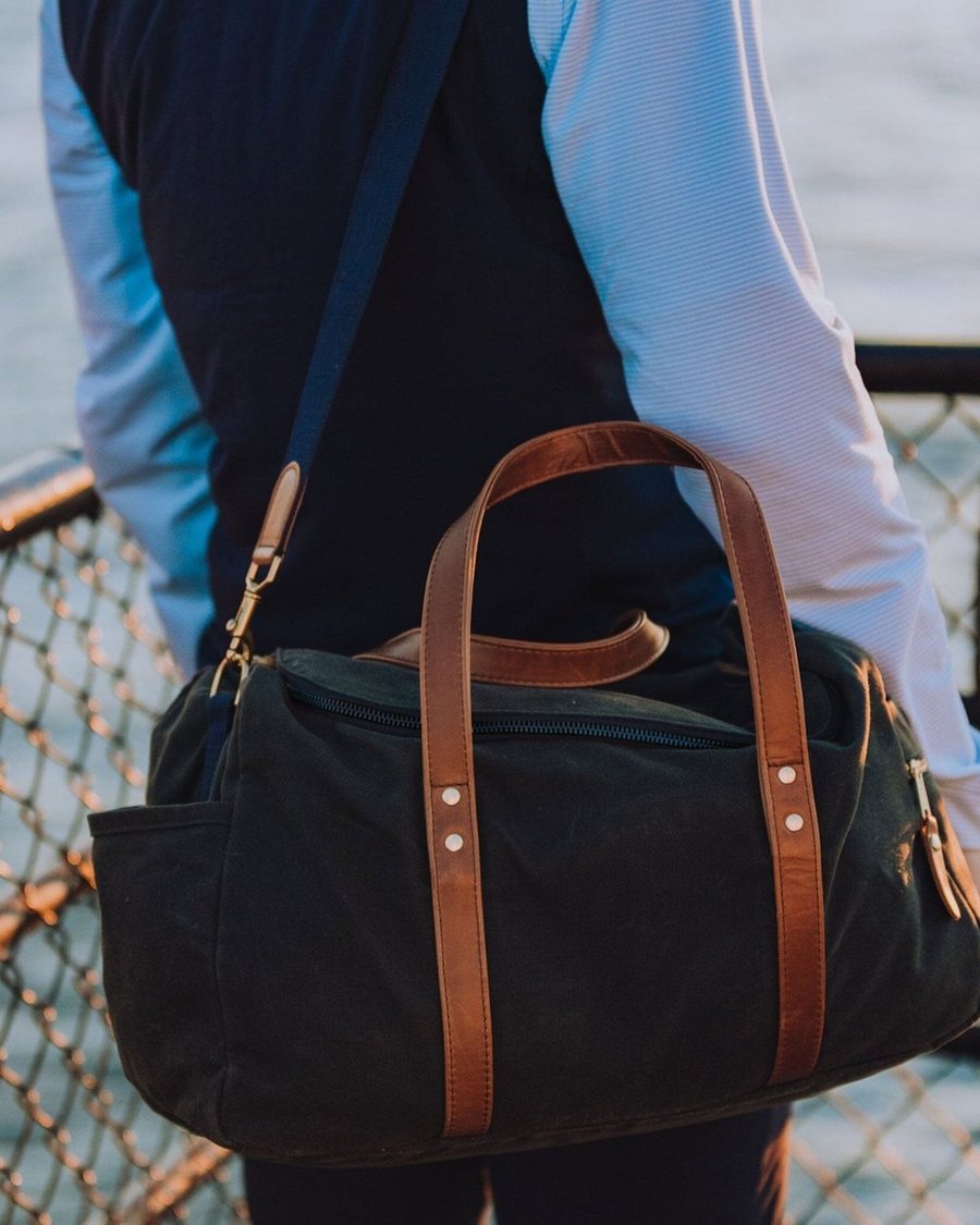 A navy Hudson Sutler duffel with leather handles carried over the shoulder