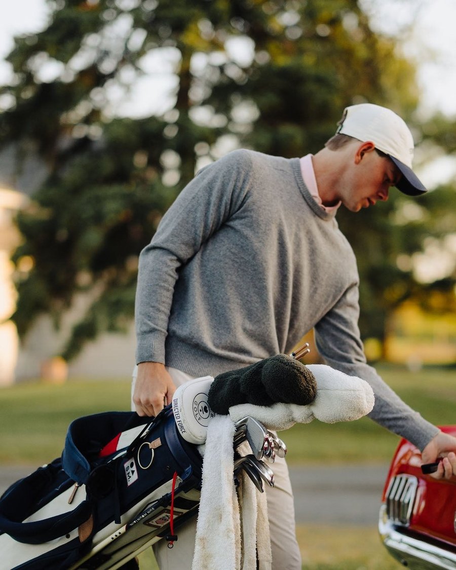 A golfer in a grey sweater pulling a club from a Sun Mountain bag