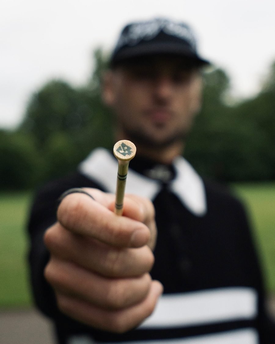 A golfer in a black No Return Club cap holding a tee toward the camera