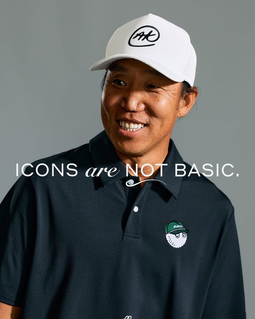 Anthony Kim smiling in a white AK cap and black polo