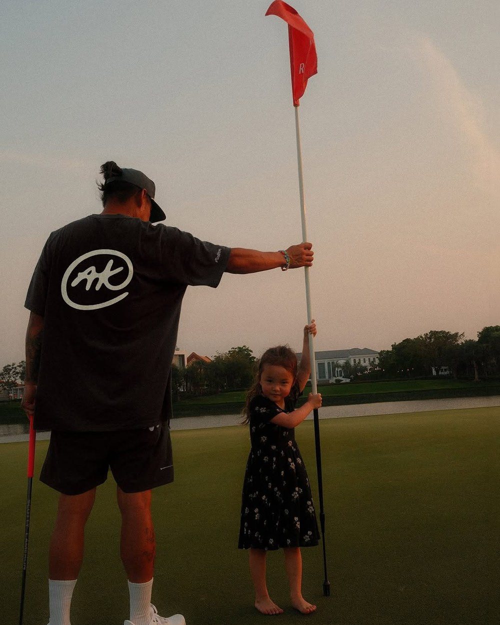 Anthony Kim in a black AK tee holding the flag with his daughter