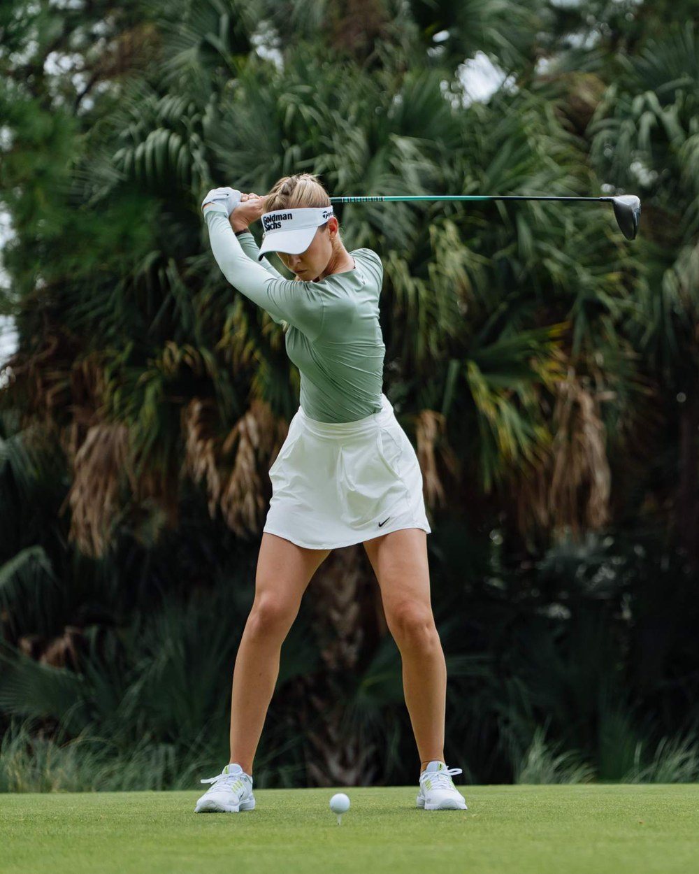 Nelly Korda at full finish in a sage mock neck and white skirt
