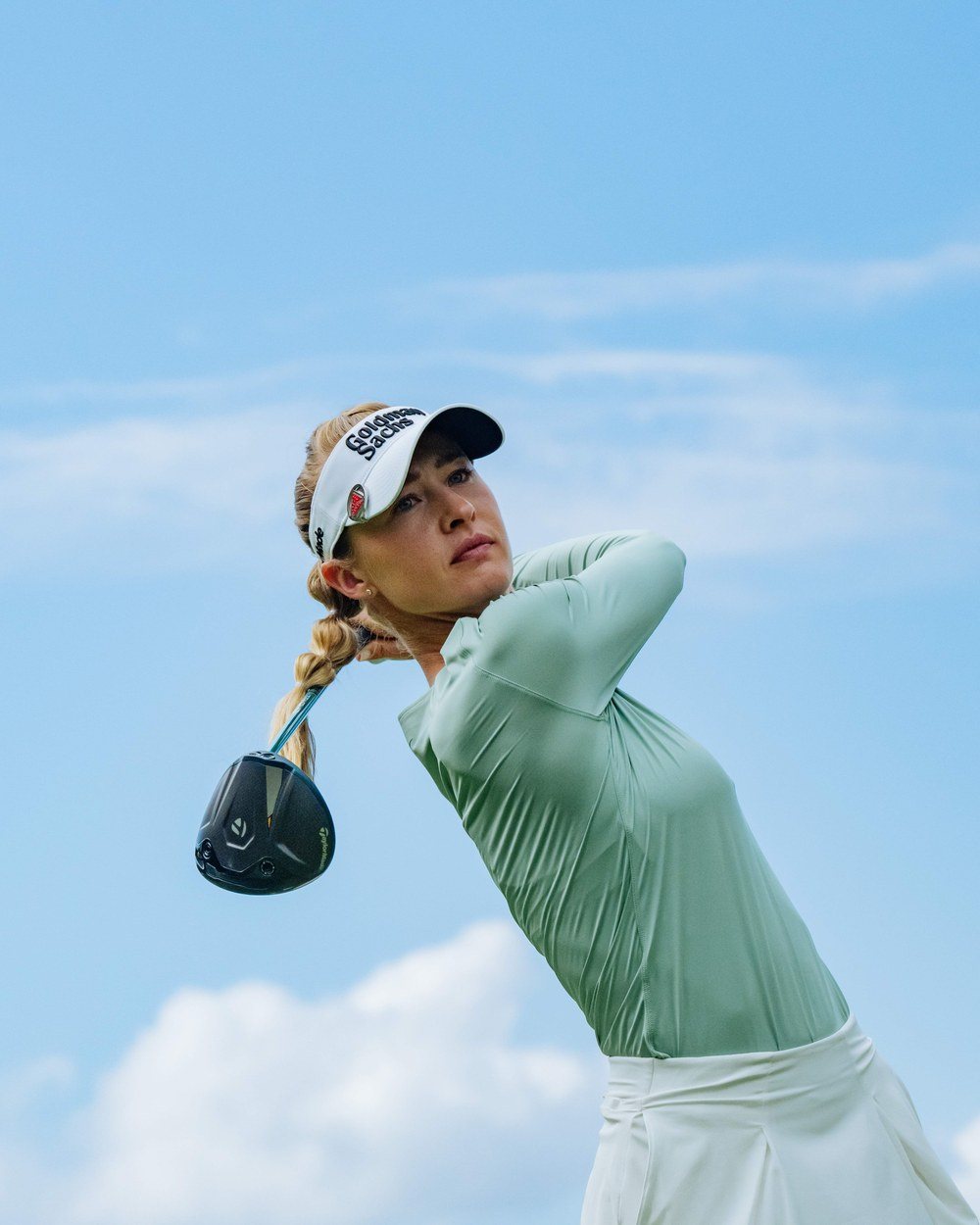 Nelly Korda holding a driver in a sage mock neck against blue sky