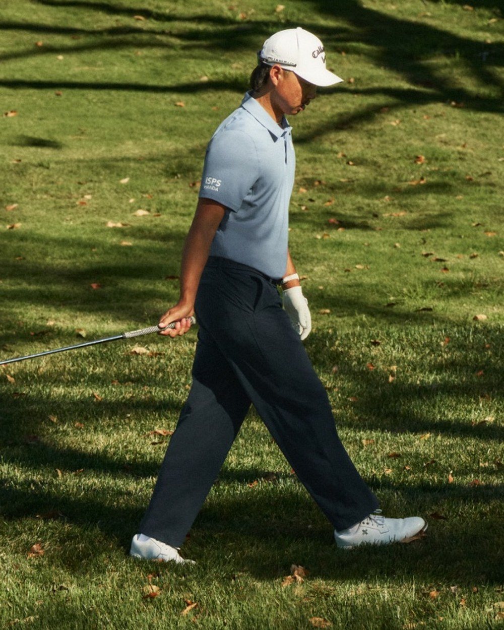 Min Woo Lee walking in a light blue polo and navy trousers