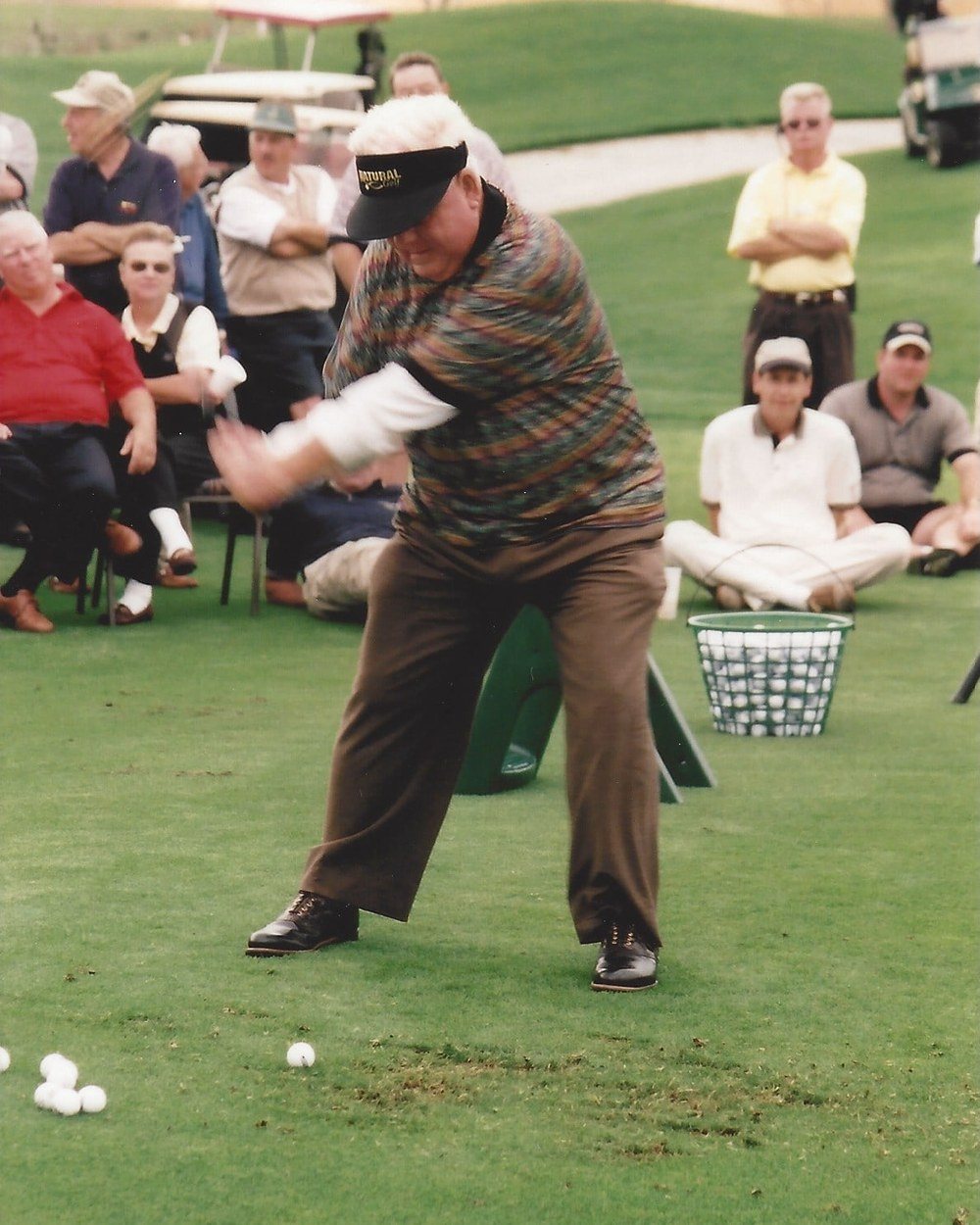 Moe Norman swinging in a patterned shirt and brown trousers in front of a crowd