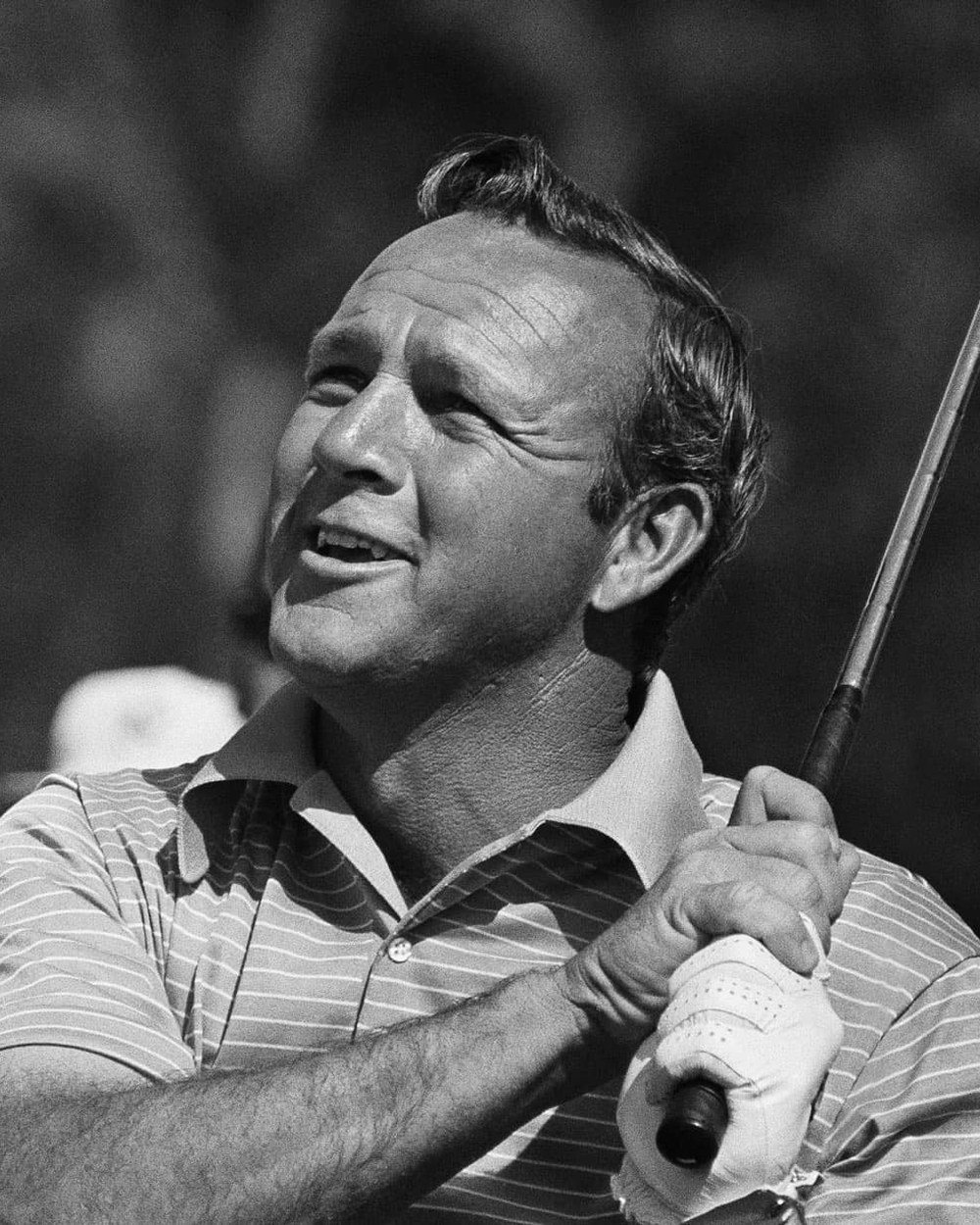 Black-and-white close-up of Arnold Palmer in a striped polo at the top of his swing