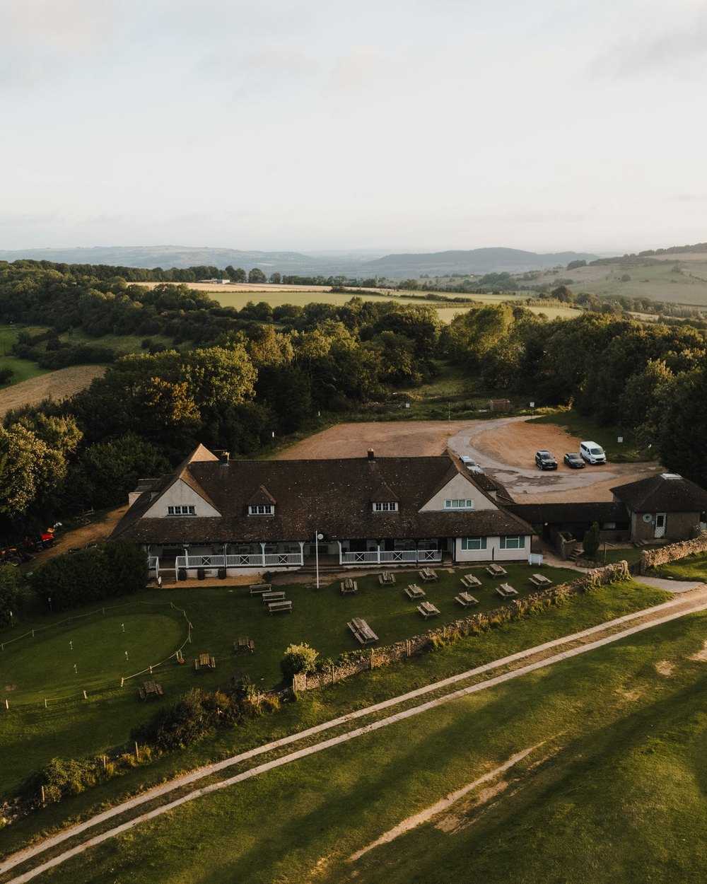An aerial view of a clubhouse surrounded by fields and woods in the English countryside