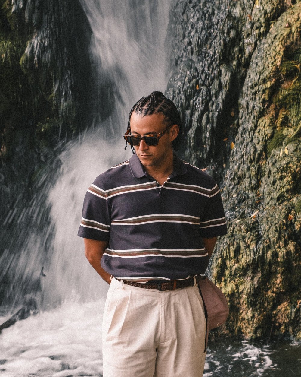 A man in the GGNC x PUMA striped polo standing in front of a waterfall