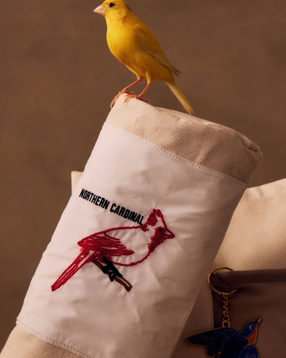 A yellow canary perched on a headcover embroidered with a northern cardinal