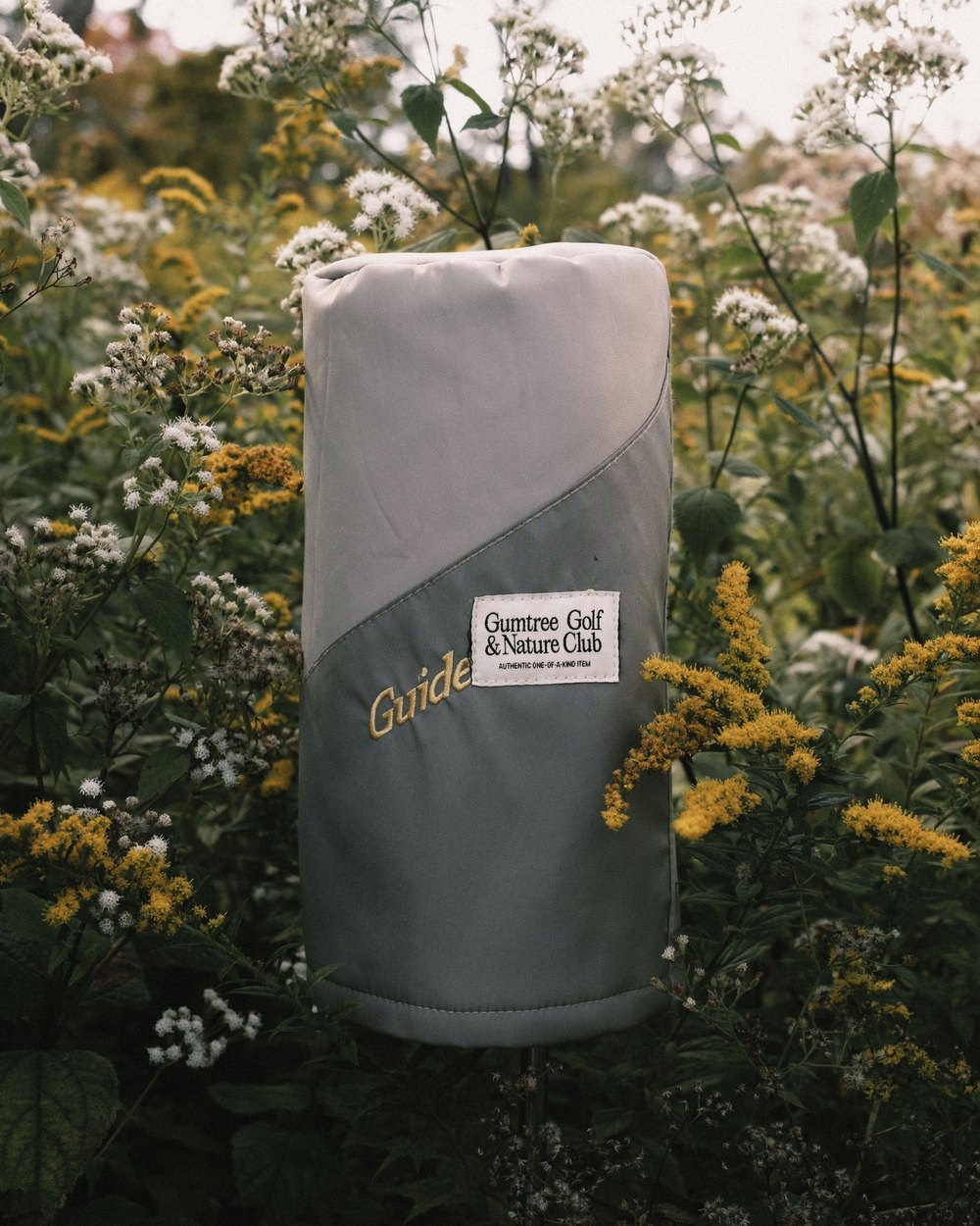 A gray headcover cut from vintage fly-fishing waders among wildflowers