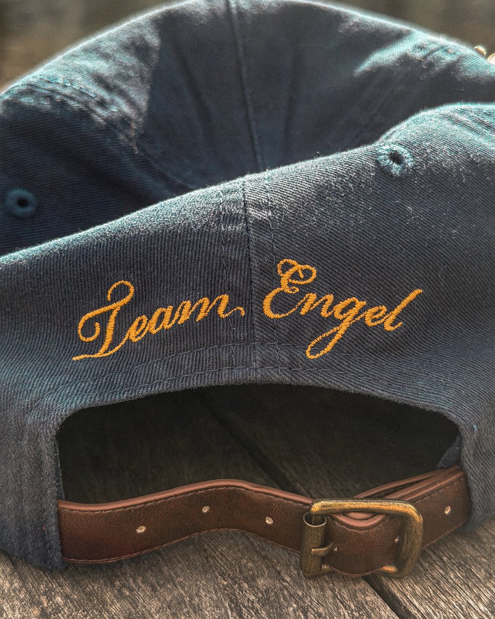 The back of a navy Team Engel cap with script embroidery and a leather strap