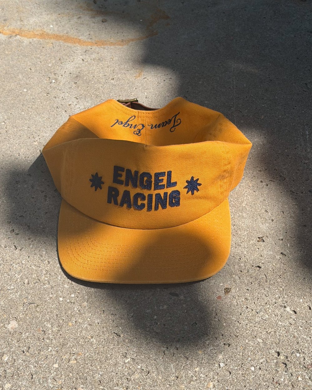 A yellow Engel Racing cap on concrete in the sun