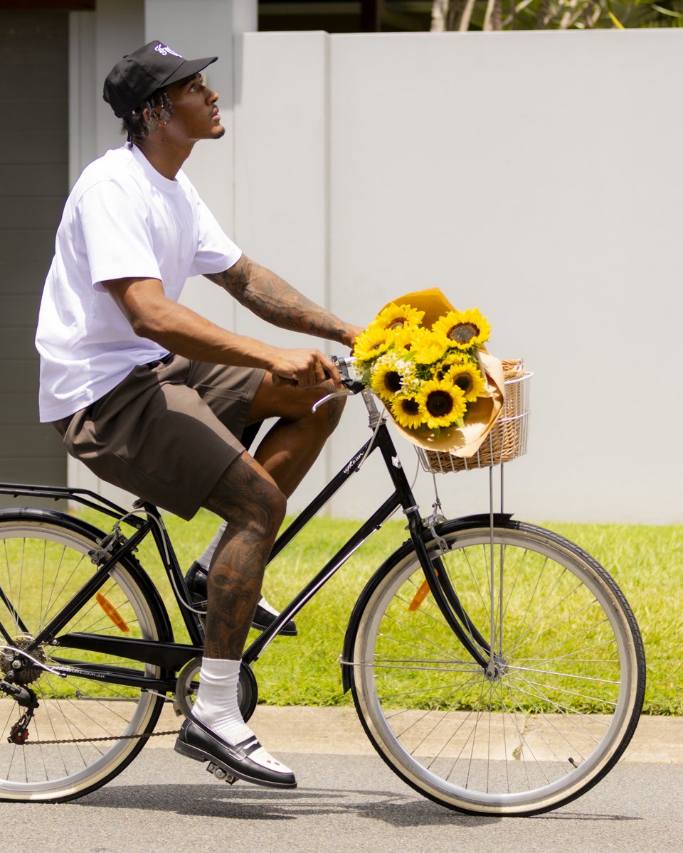 A man in a cap riding a bicycle with sunflowers in the basket