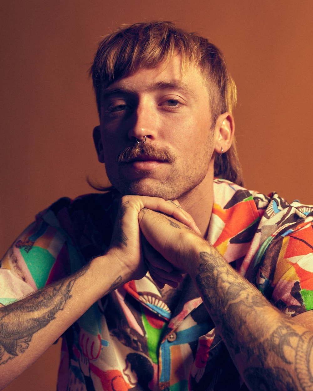 Freddy Tyler Paul in a printed shirt against an orange wall