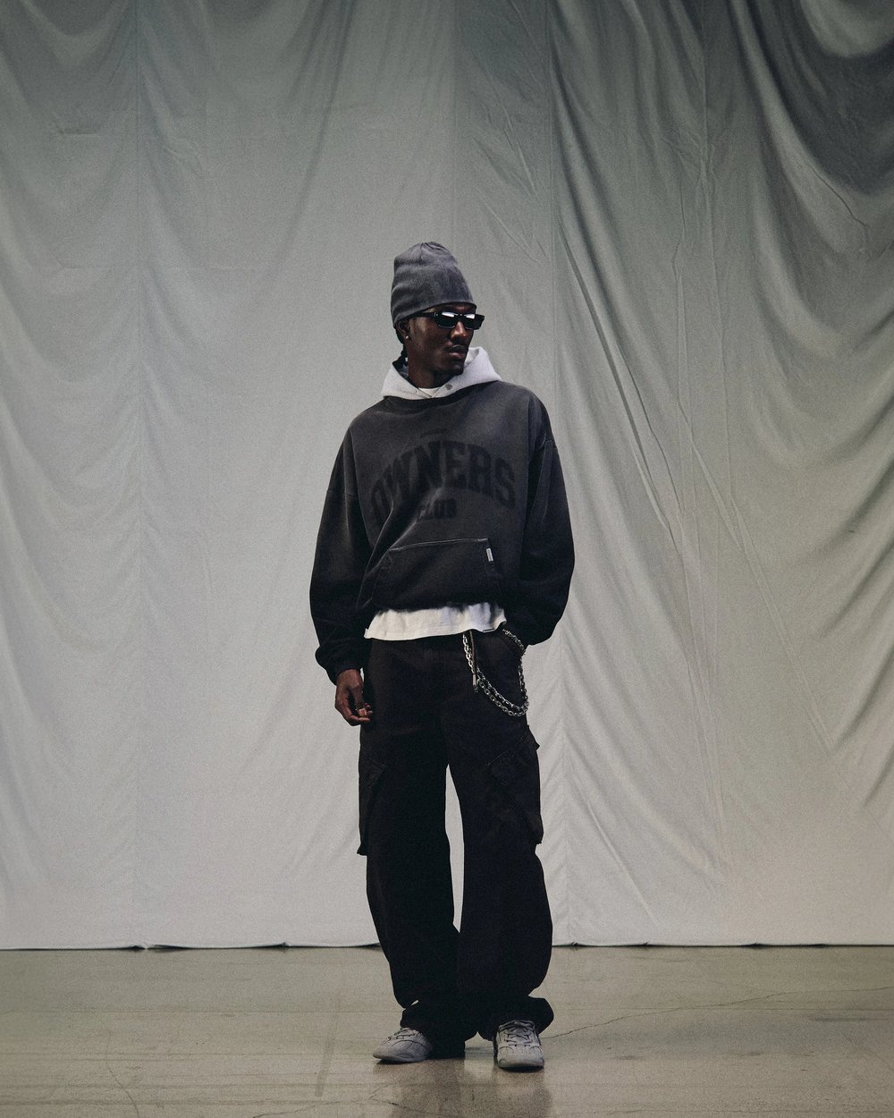 A man in a beanie and black Owners Club hoodie in a white studio