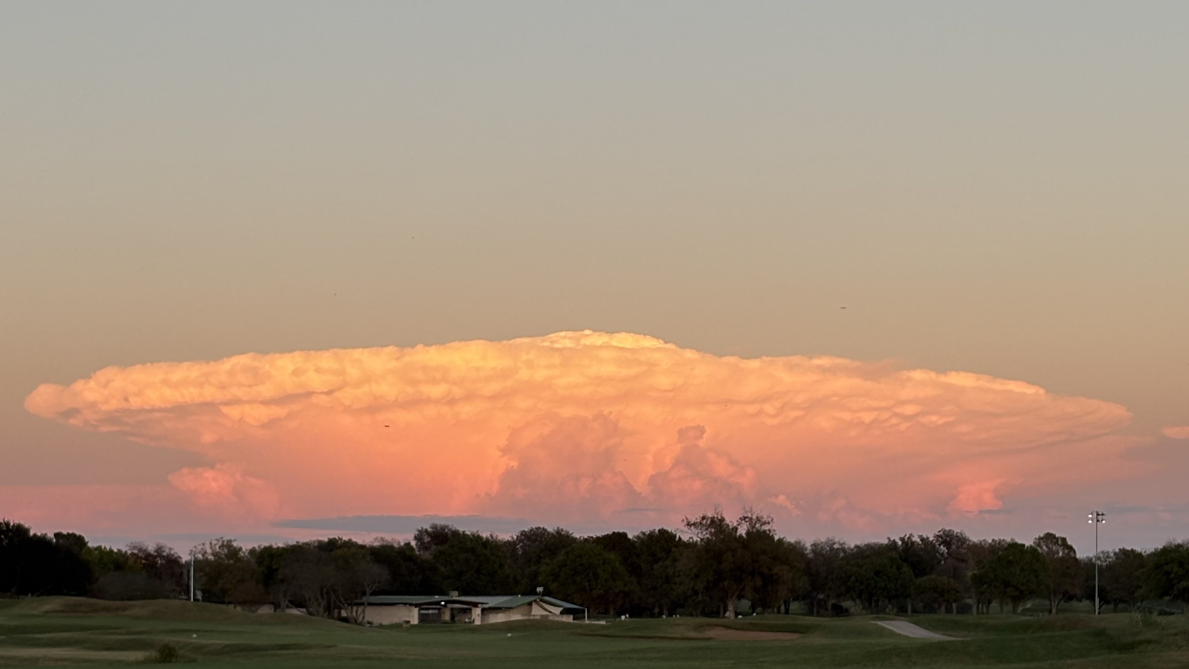 A Texas thunderhead glowing pink at sunset above an Austin municipal golf course