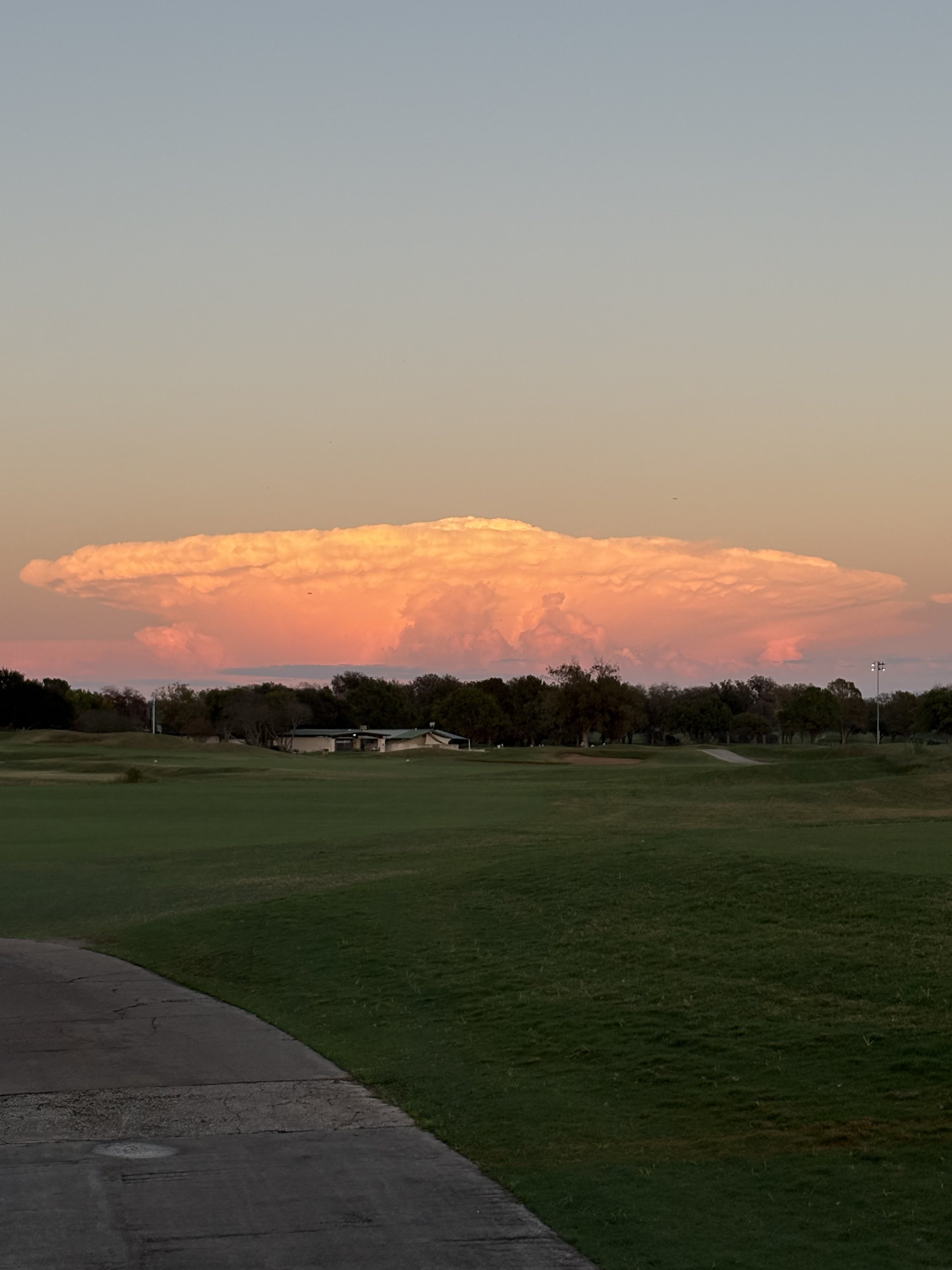 A Texas thunderhead glowing pink at sunset above an Austin municipal golf course