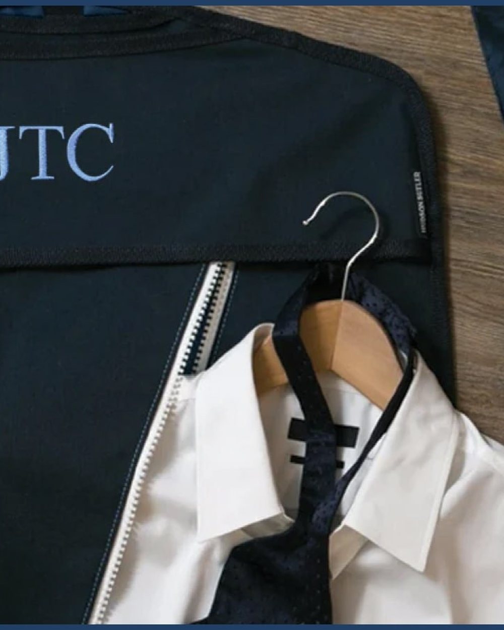 A navy garment bag monogrammed JTC with a white shirt on a hanger