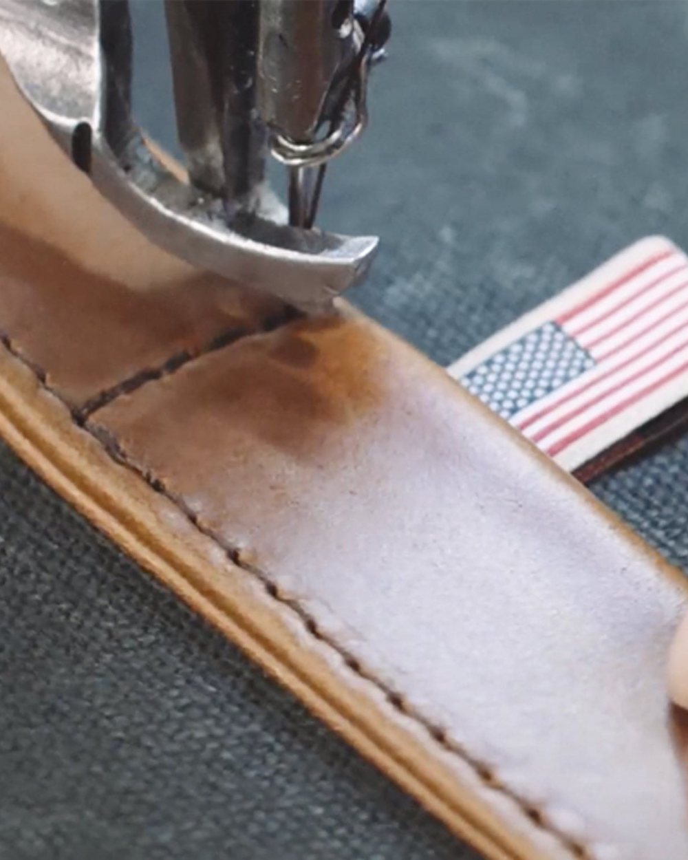 A leather handle being stitched onto waxed canvas beside an American flag label