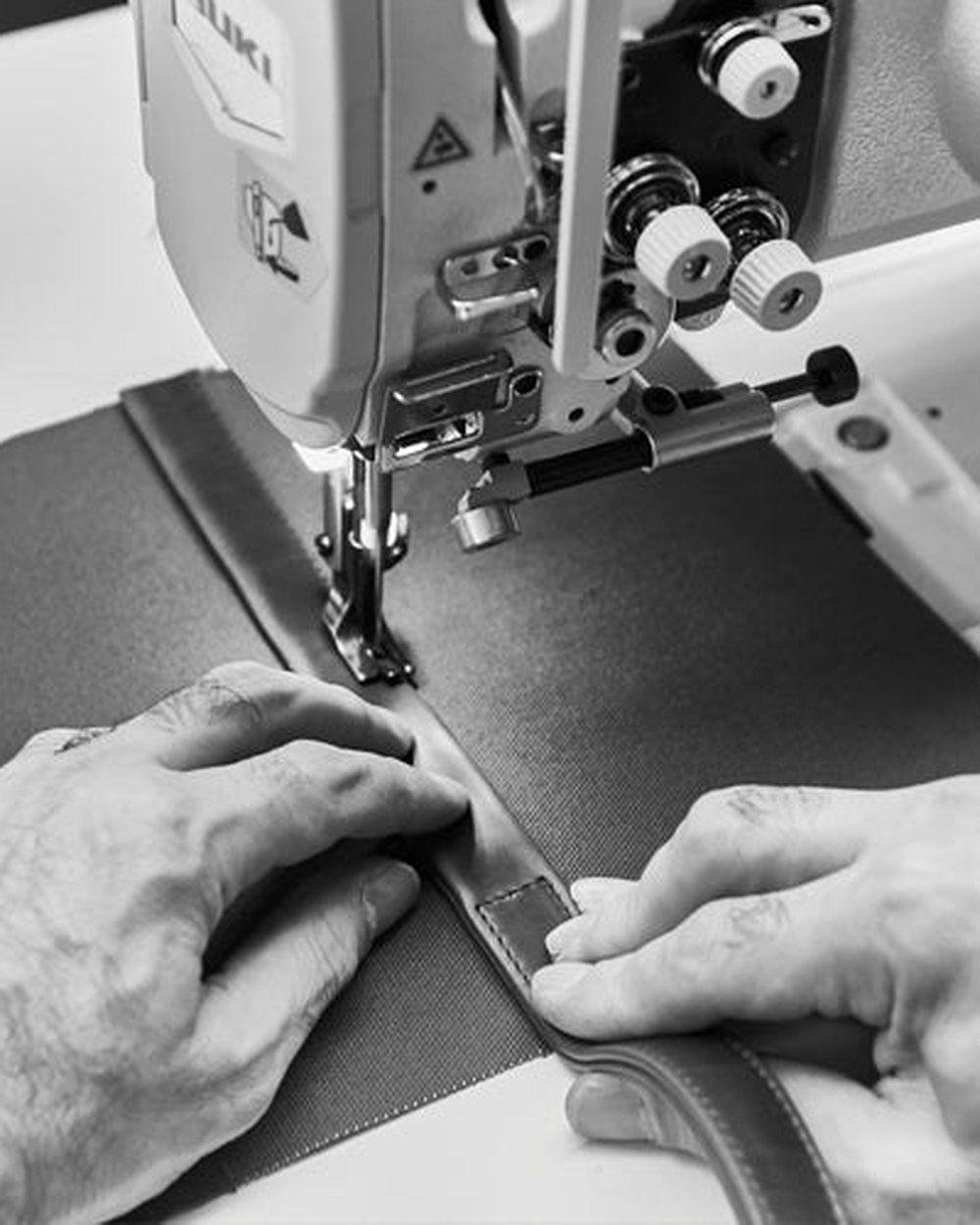 Hands guiding leather through a sewing machine