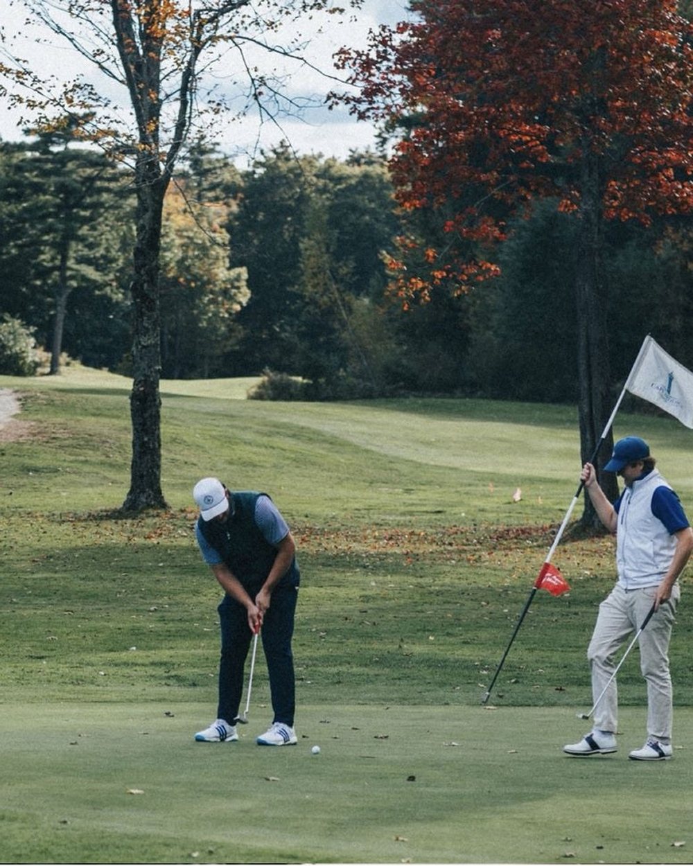 Two golfers on a green in autumn with trees behind