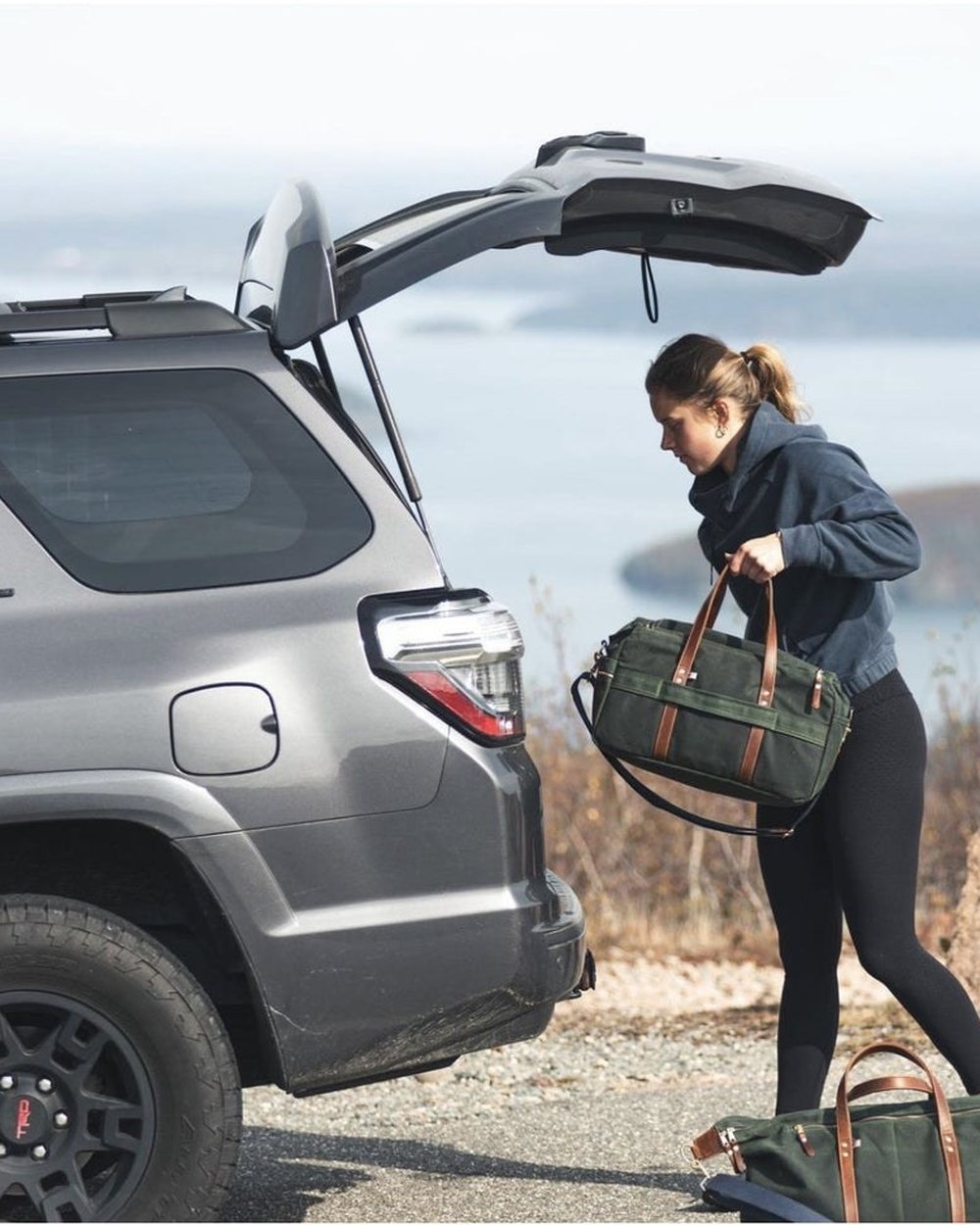 A woman lifting a Hudson Sutler duffel out of the back of an SUV