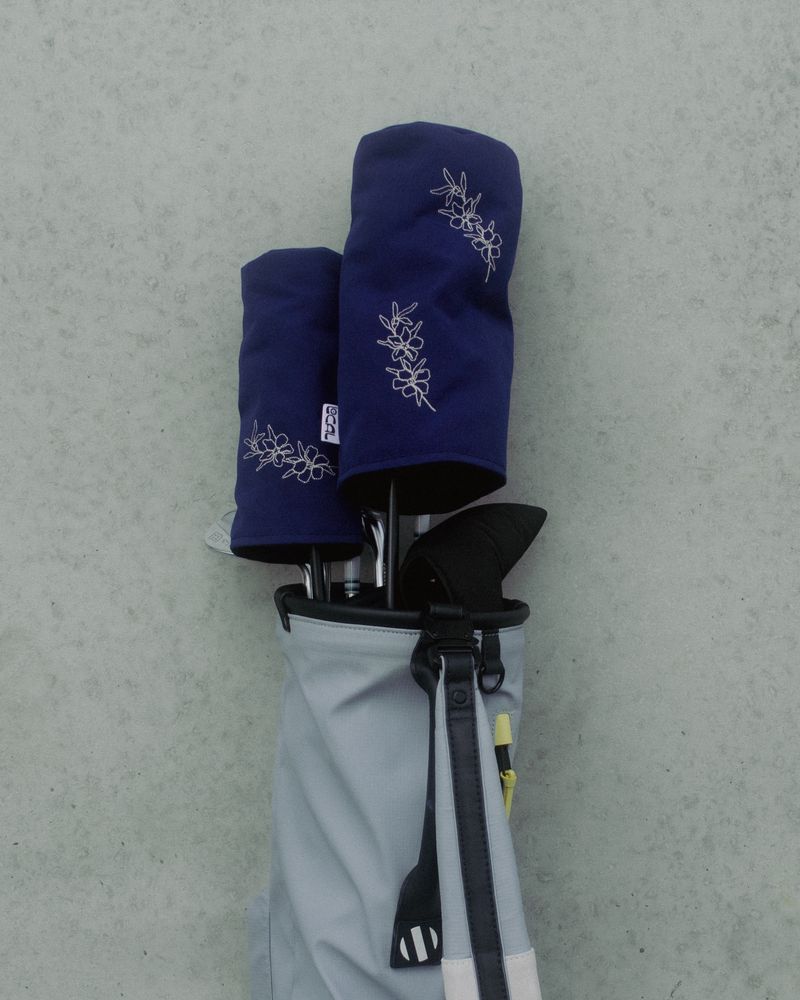 Two navy canvas headcovers with scattered manuka embroidery in a golf bag