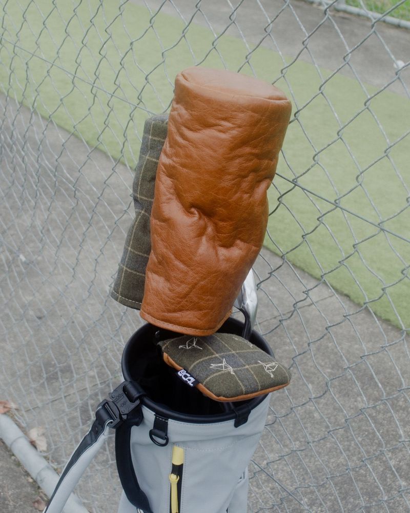 A tan leather headcover on a driver in a golf bag beside a fence