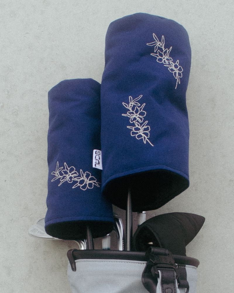 Navy manuka headcovers in a grey golf bag against a wall