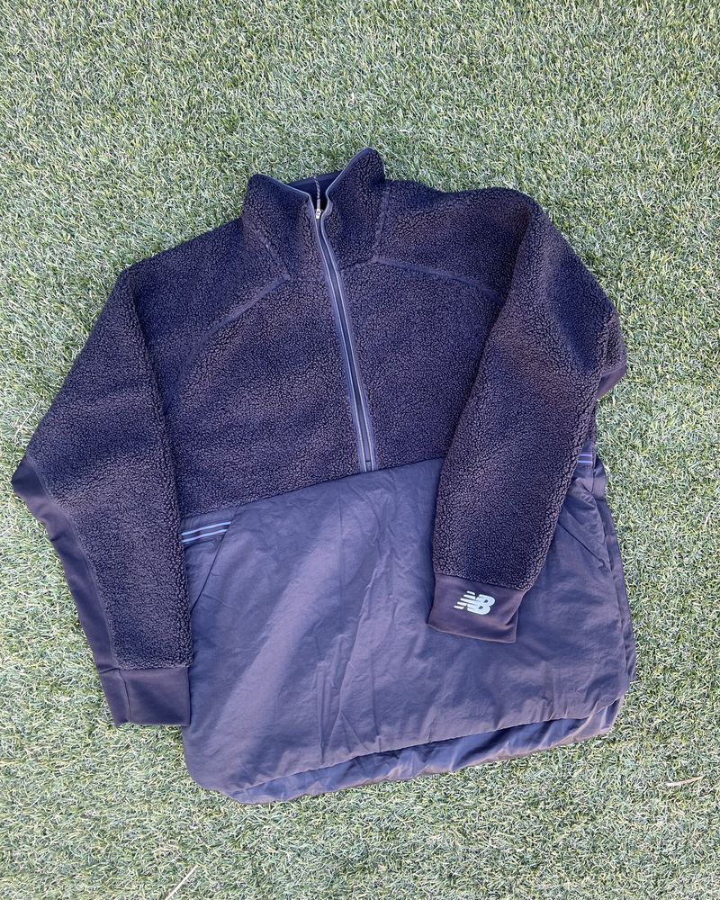 A navy New Balance fleece running jacket laid on grass
