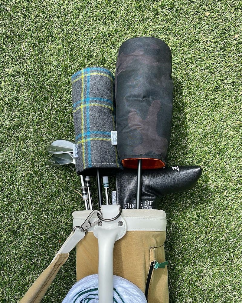 Tartan and oilskin headcovers in a golf bag on artificial turf