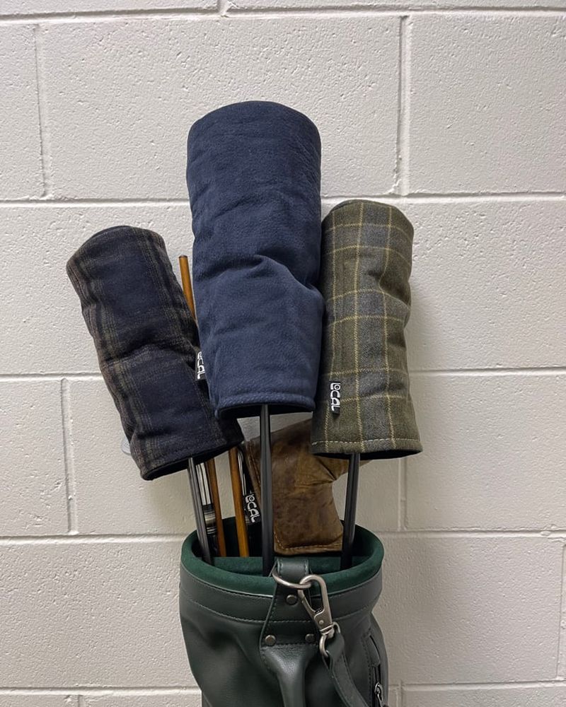 Navy and tartan wool headcovers in a green carry bag against a white wall