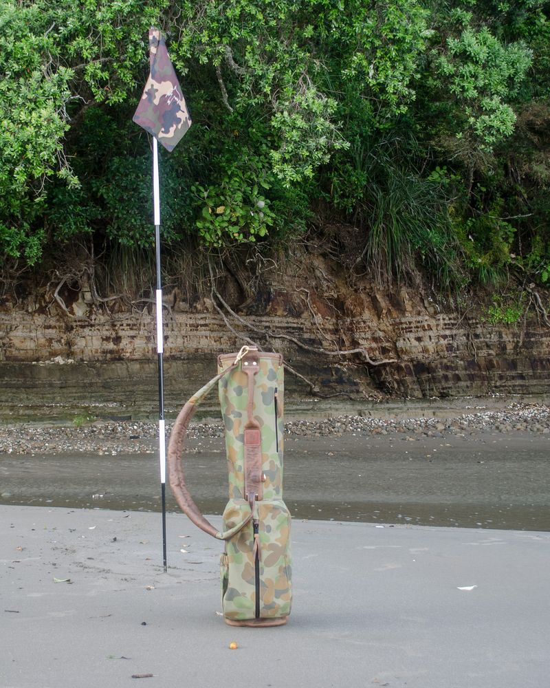 The camo Sunday bag standing on a tidal beach in Orewa beside a flagstick