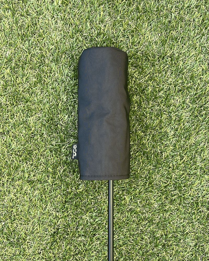 A black sailcloth headcover on a club on turf