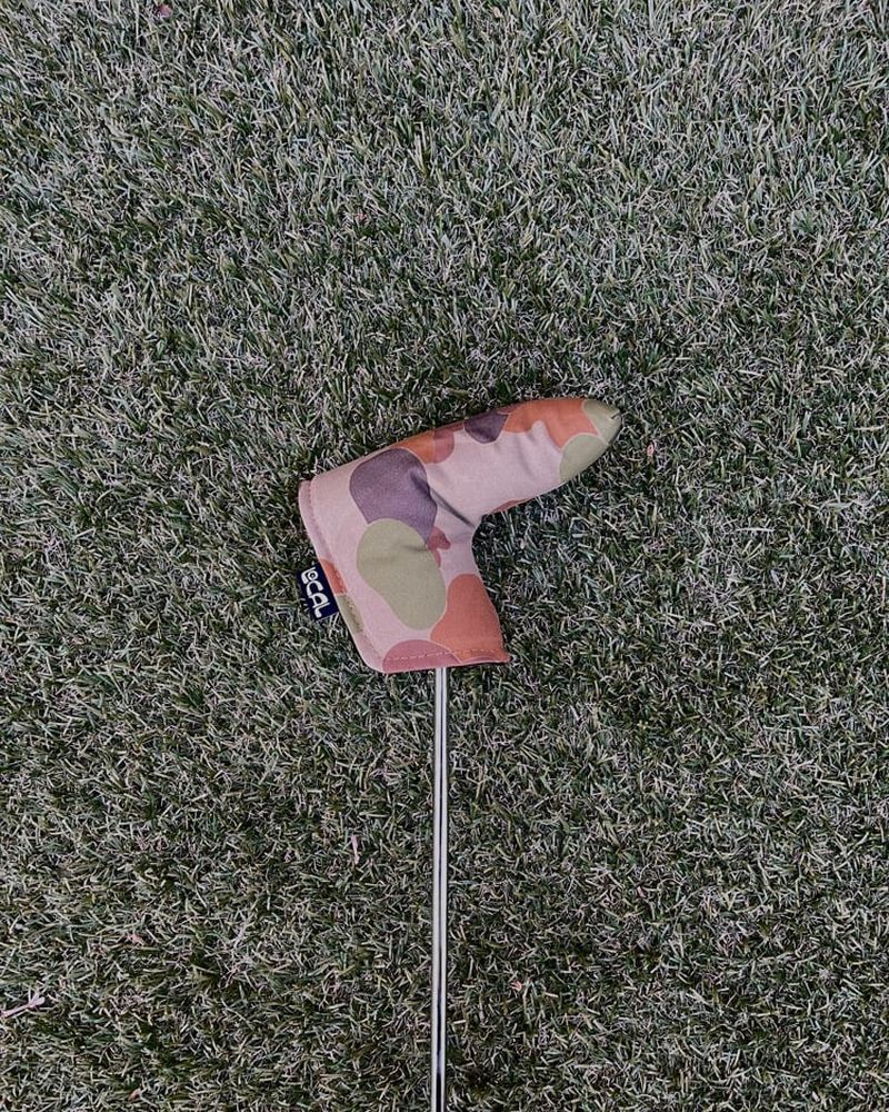 A camo putter cover on a putter lying on grass