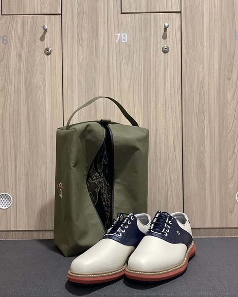 An olive Local GC shoe bag with saddle shoes on a locker room bench