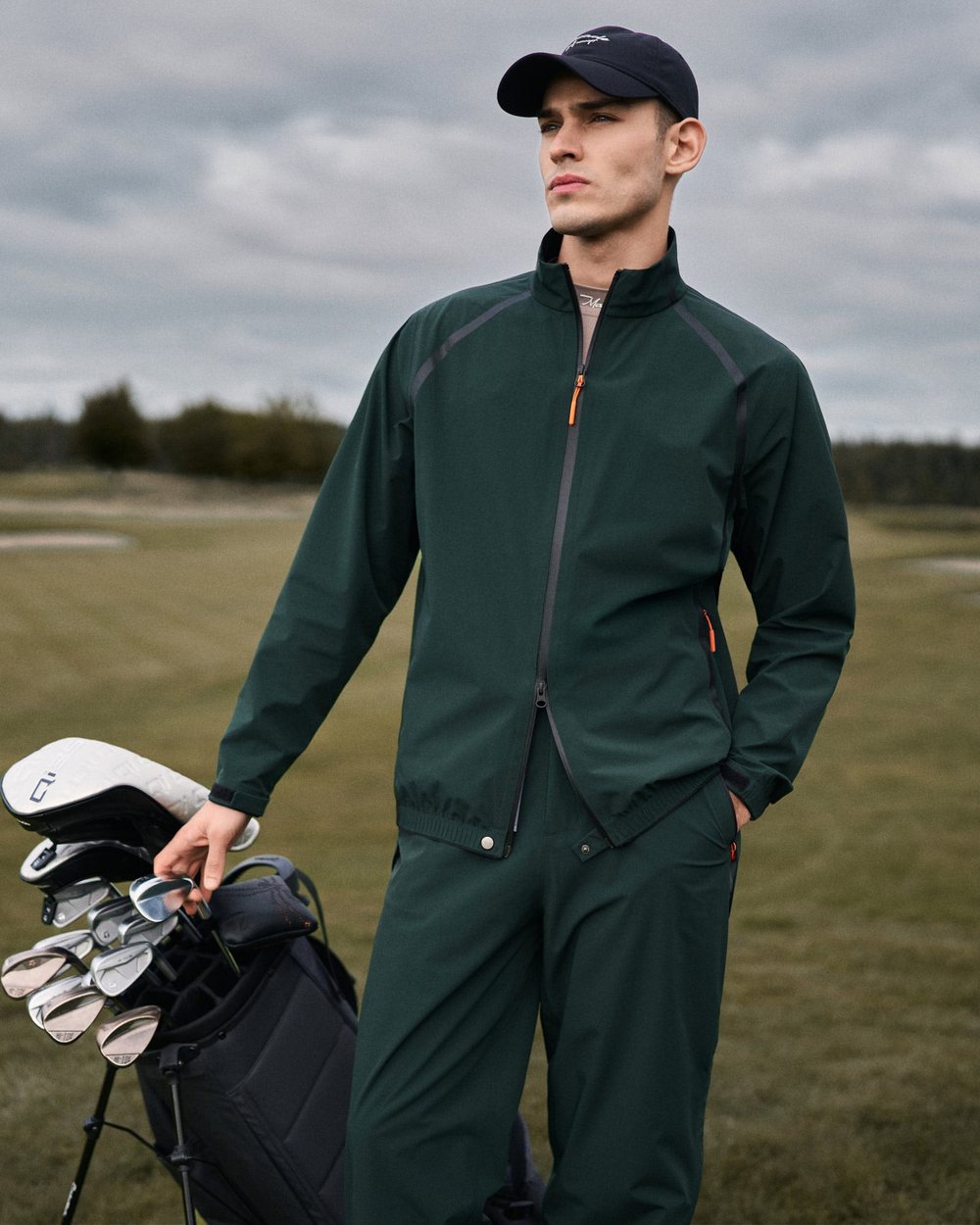 A golfer in a green Macade HydroCore rain suit beside a stand bag on the course