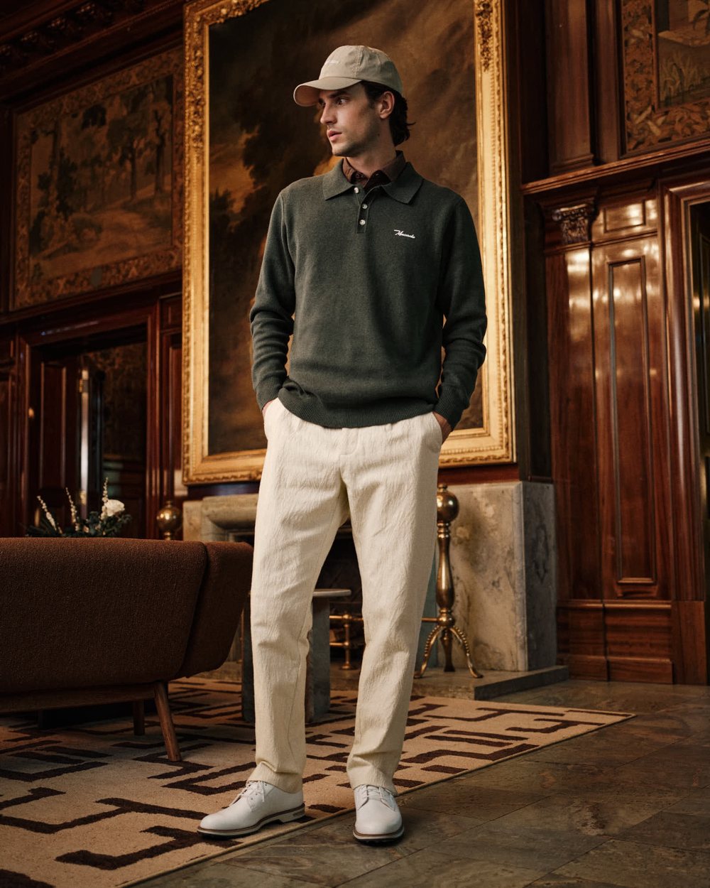 A man in a dark green Macade knit polo and cream trousers in a wood-panelled room