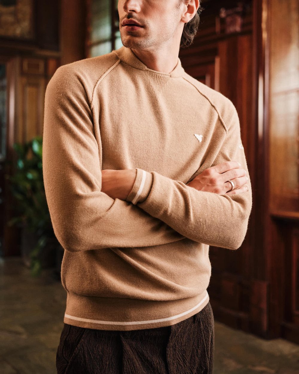 A man in a camel Macade Flow Light bomber-neck knit with arms crossed