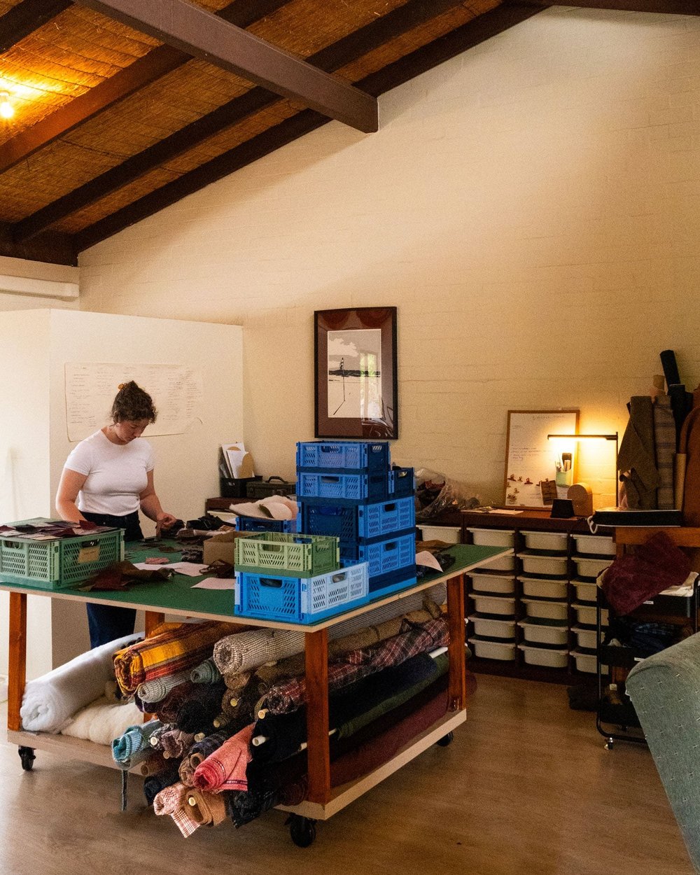 A worktable in the studio with boxes of fabric and finished pieces
