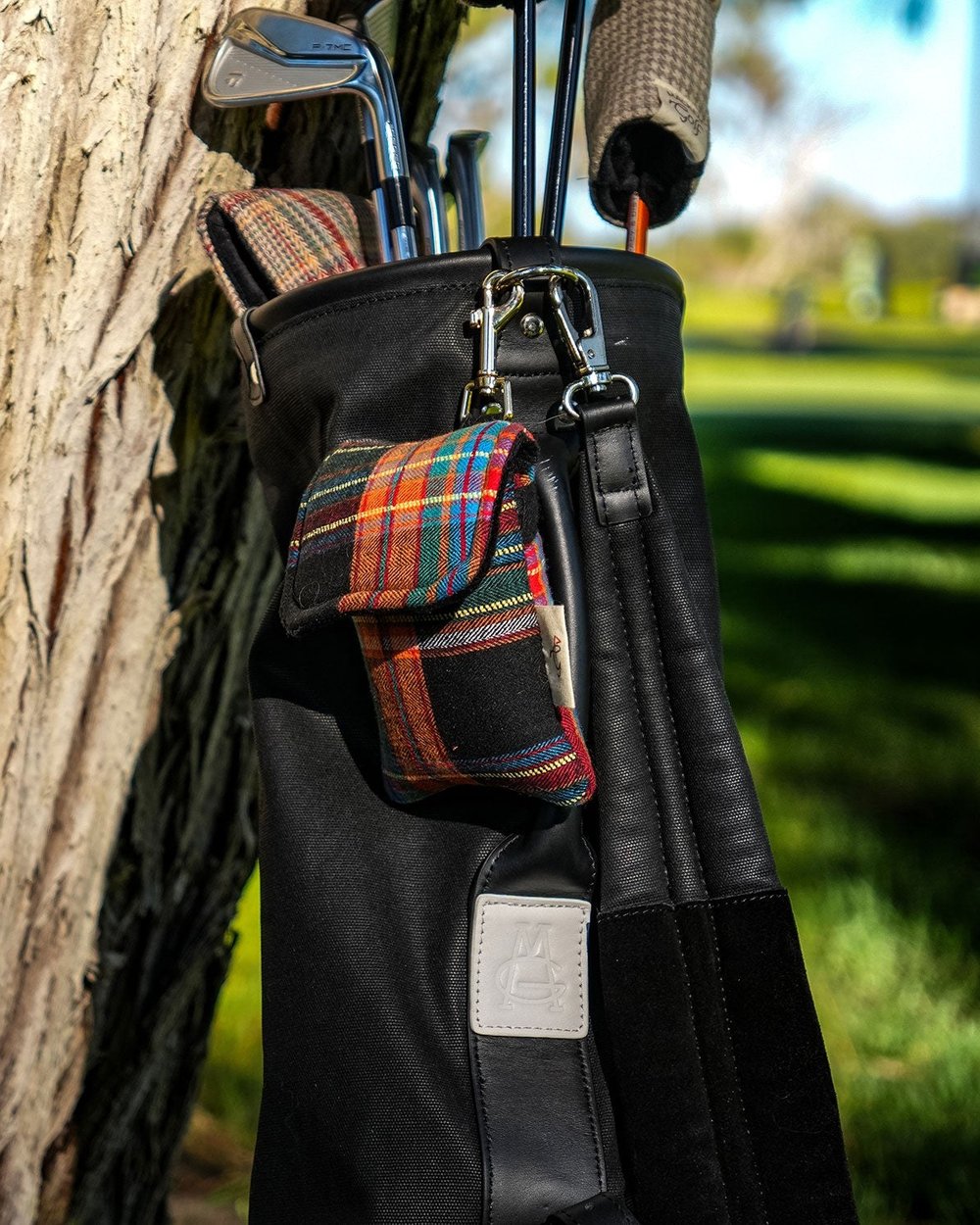 A tartan pouch clipped to a black golf bag in the late sun