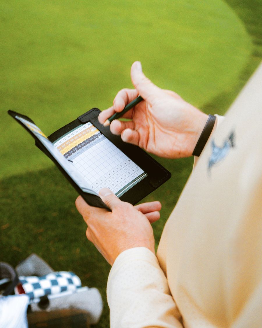 A golfer writing his score in a Magpie leather scorecard holder