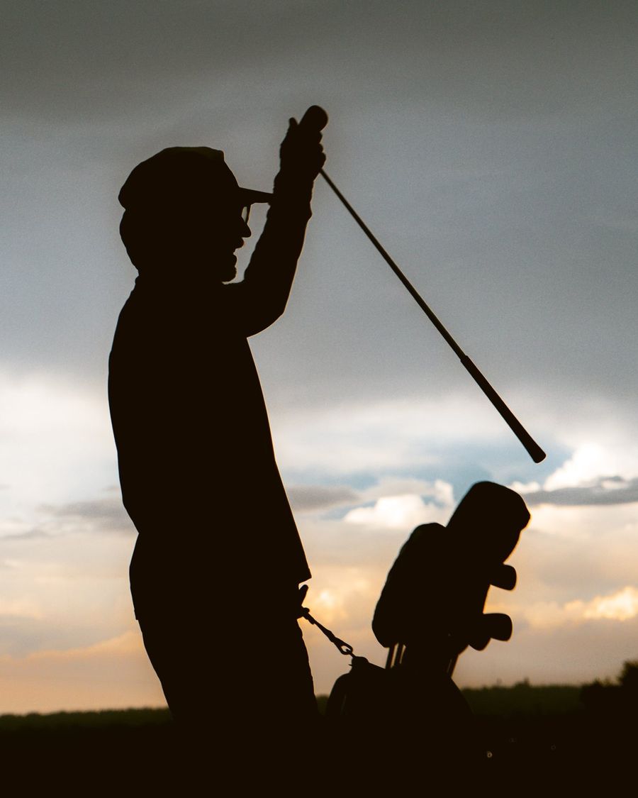 A golfer silhouetted at the top of his swing at sunset
